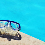 Eine Taucherbrille liegt auf einem Schwimmbeckenrand. Im Hintergrund sieht man blaues Wasser.